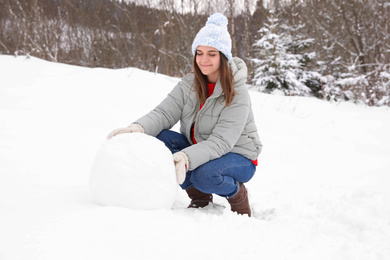 Happy woman making ball for snowman outdoors. Winter vacation