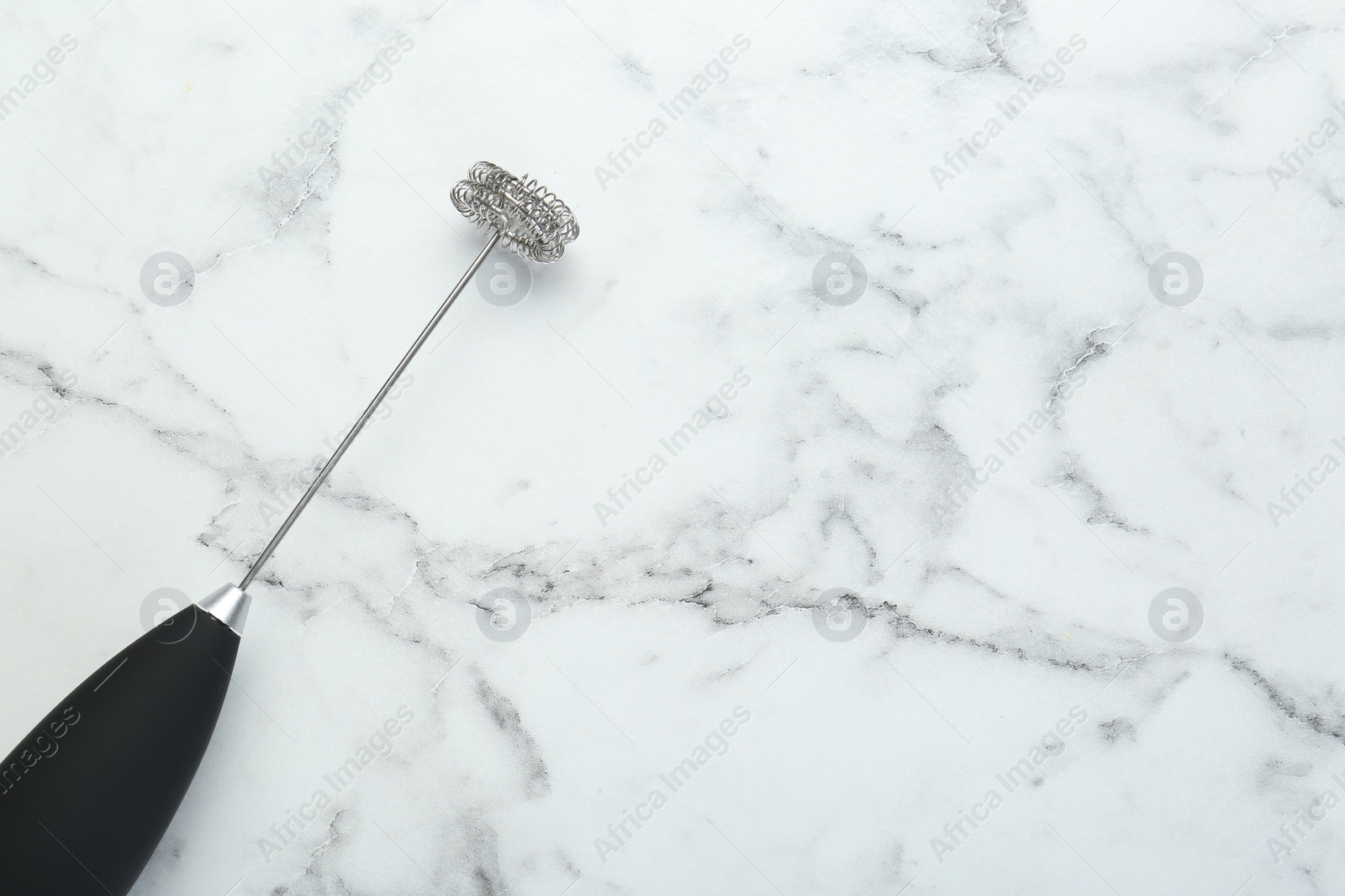 Photo of Black milk frother wand on white marble table, top view. Space for text