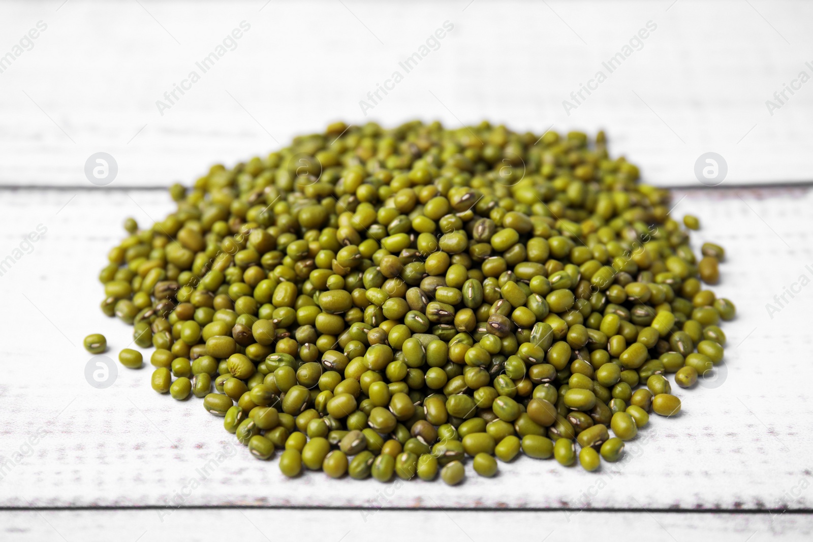 Photo of Pile of green mung beans on white wooden table, closeup