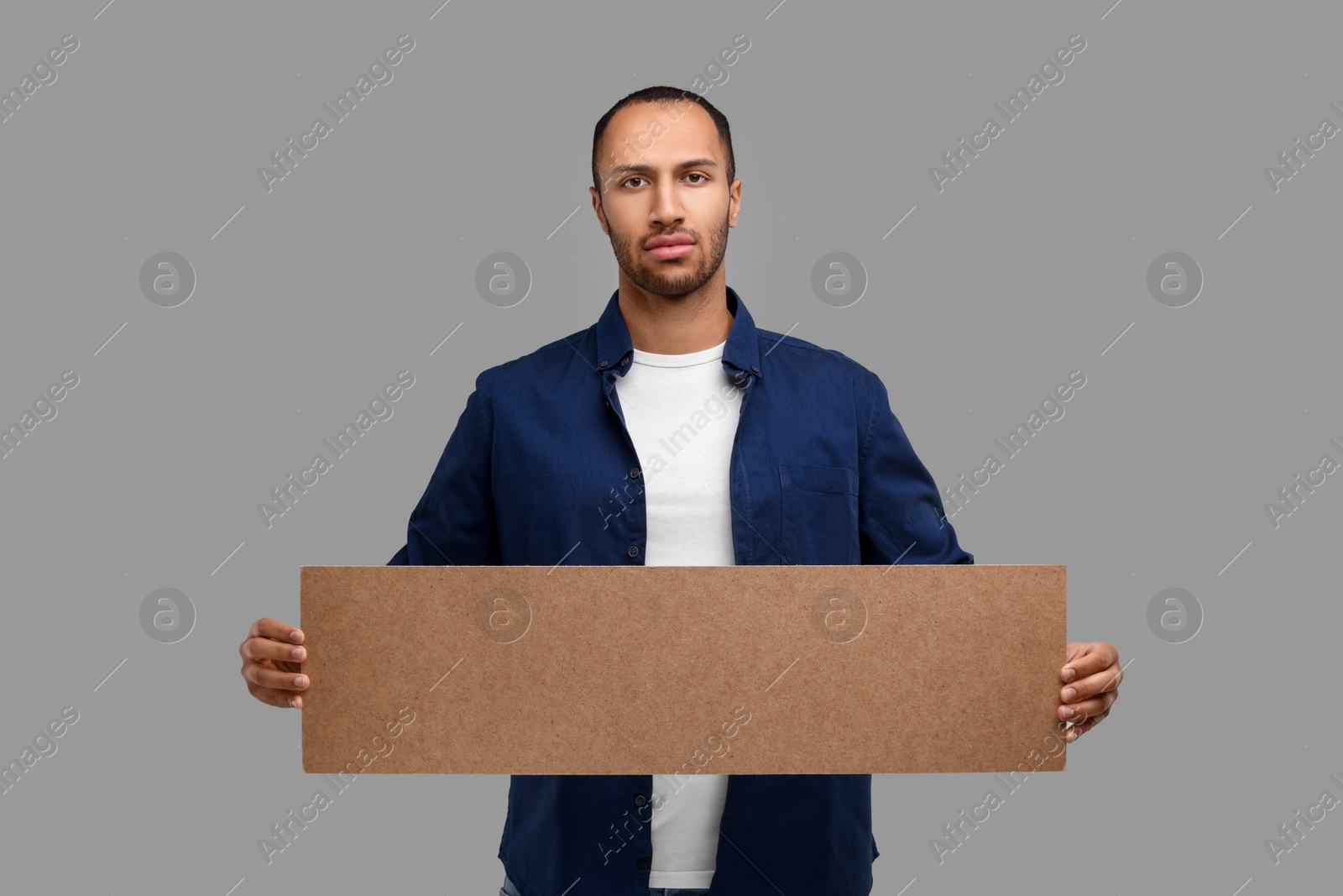 Photo of Man holding blank cardboard banner on grey background, space for text