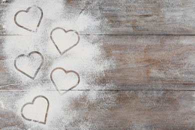 Photo of Heart shapes made of flour on wooden table, top view. Space for text