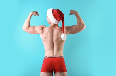 Photo of Young muscular man in Santa hat on color background