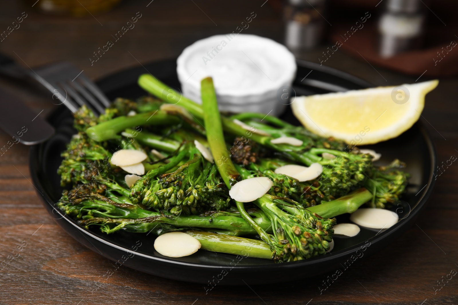 Photo of Tasty cooked broccolini with almonds, lemon and sauce on wooden table, closeup