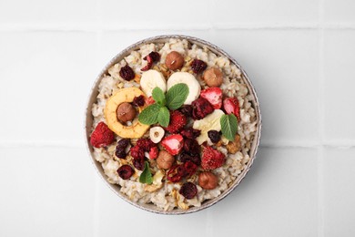 Photo of Oatmeal with freeze dried fruits, nuts and mint on white tiled table, top view