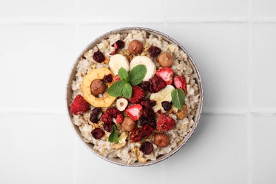 Oatmeal with freeze dried fruits, nuts and mint on white tiled table, top view