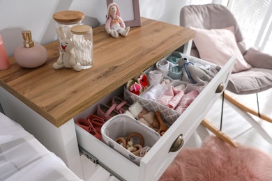 Photo of Modern open chest of drawers with baby clothes and accessories in room, closeup