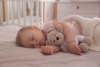 Photo of Adorable little baby with toy bear sleeping on bed at home