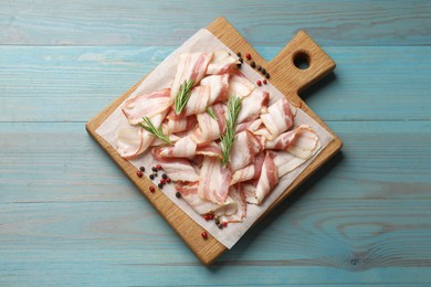 Slices of raw bacon and spices on light blue wooden table, top view