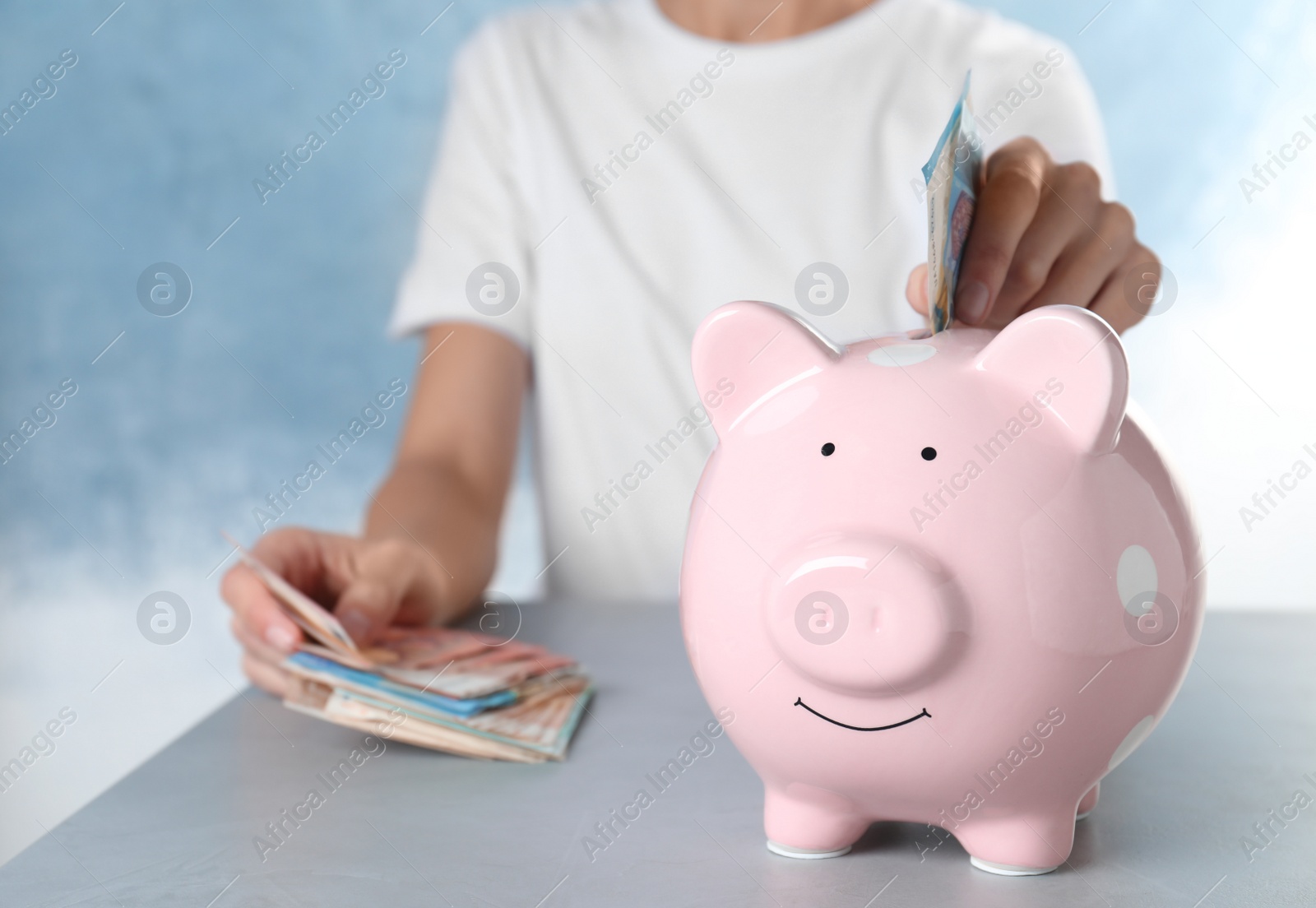 Photo of Woman putting Euro banknote into piggy bank at table indoors, closeup. Money savings