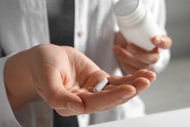 Woman holding pill and bottle on blurred background, closeup