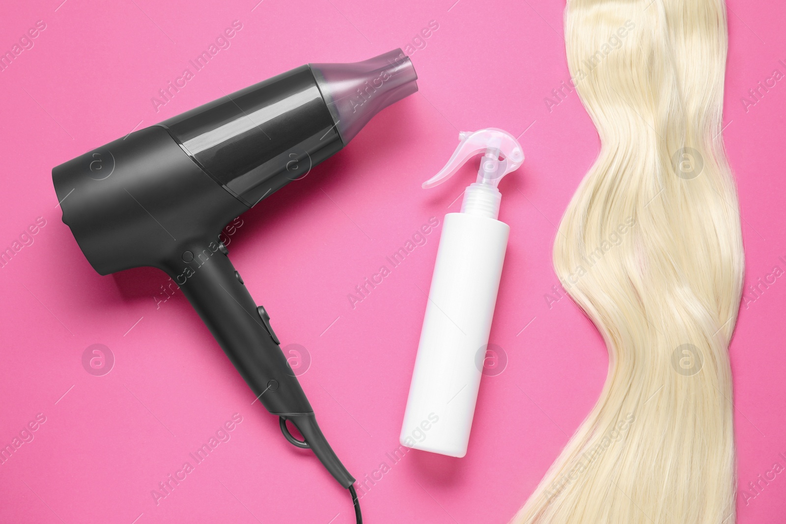 Photo of Spray bottle with thermal protection, stylish hairdryer and lock of blonde hair on pink background, flat lay