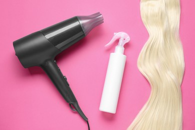 Photo of Spray bottle with thermal protection, stylish hairdryer and lock of blonde hair on pink background, flat lay
