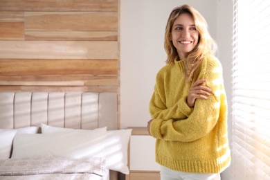 Photo of Beautiful young woman wearing warm yellow sweater near window at home. Space for text