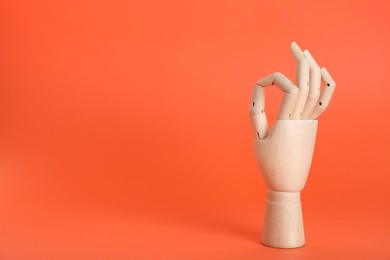 Wooden mannequin hand showing okay gesture on orange background. Space for text