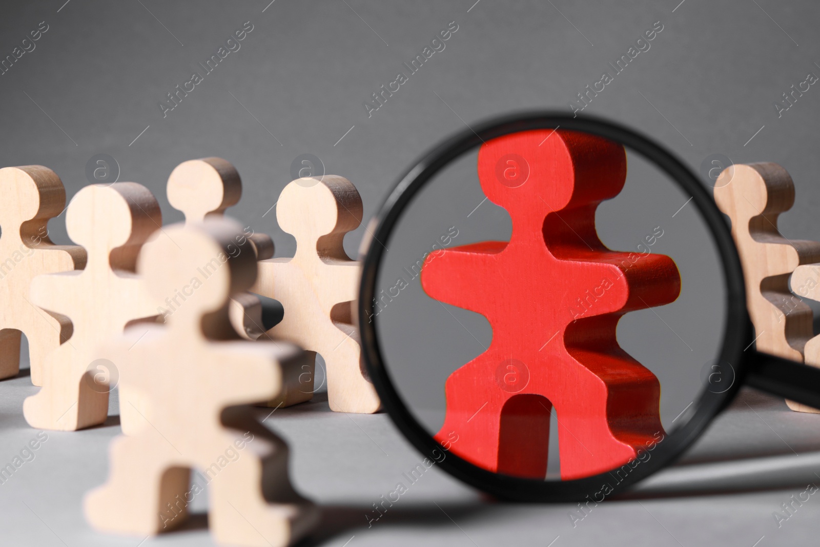 Photo of Magnifying glass near red pawn among wooden ones on light grey background, closeup. Recruiter searching employee