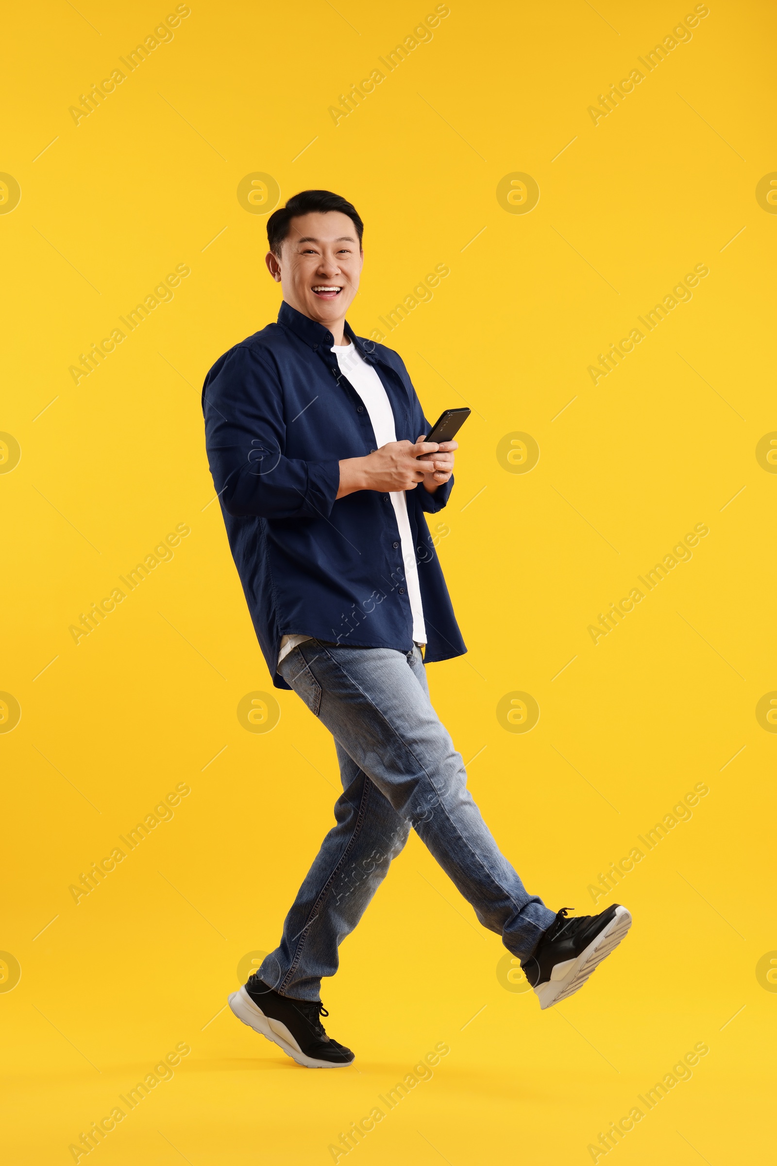 Photo of Full length portrait of happy man with smartphone on yellow background