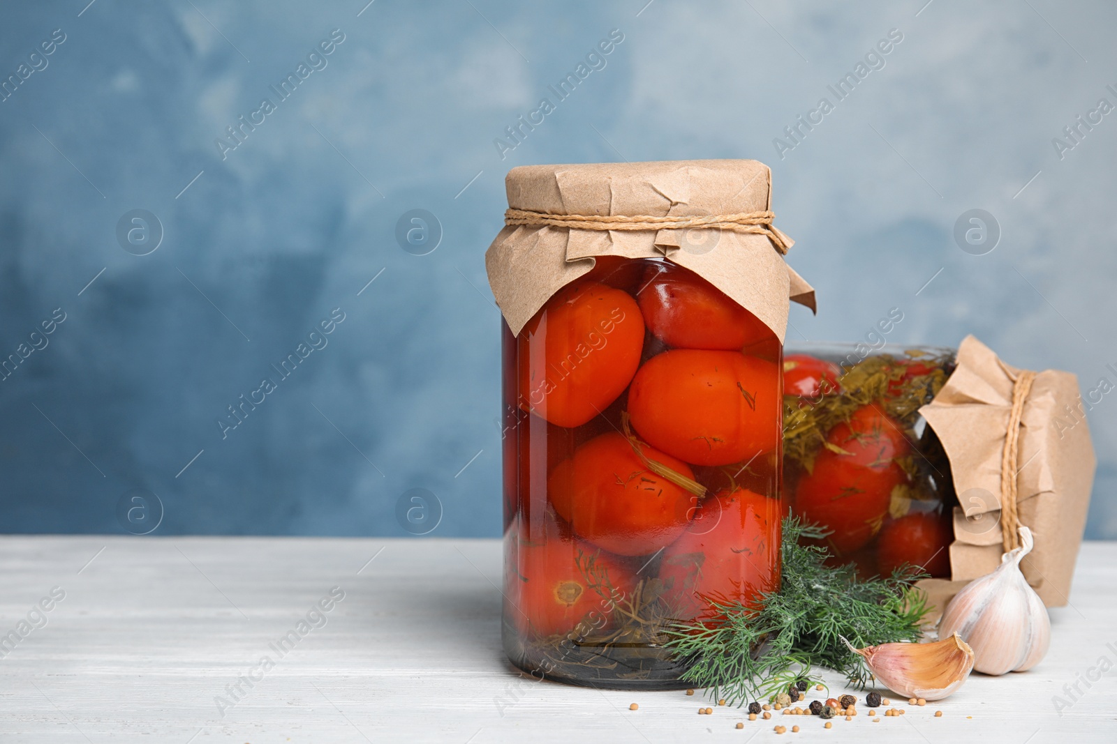 Photo of Pickled tomatoes in glass jars and products on white wooden table against blue background, space for text