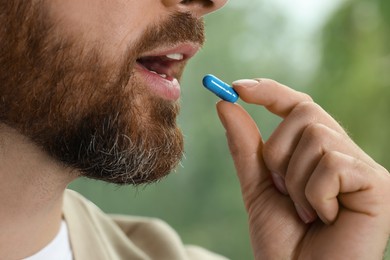 Closeup view of bearded man taking pill on blurred background