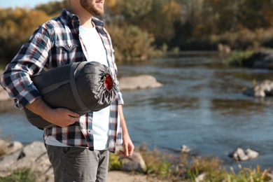 Photo of Male camper with sleeping bag near pond. Space for text