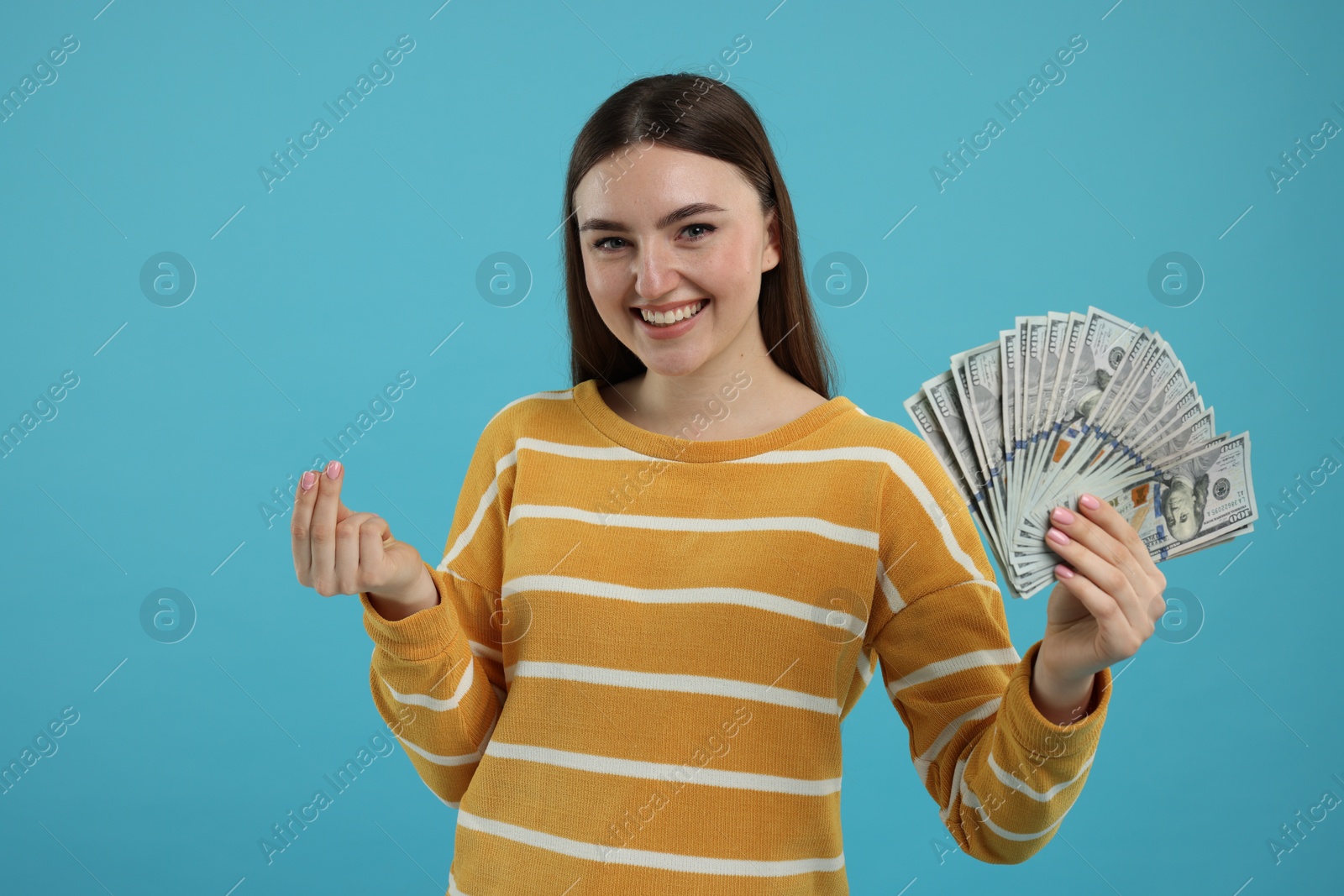 Photo of Happy woman with dollar banknotes showing money gesture on light blue background