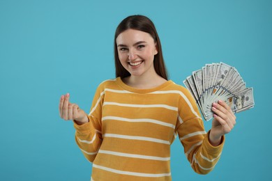 Photo of Happy woman with dollar banknotes showing money gesture on light blue background