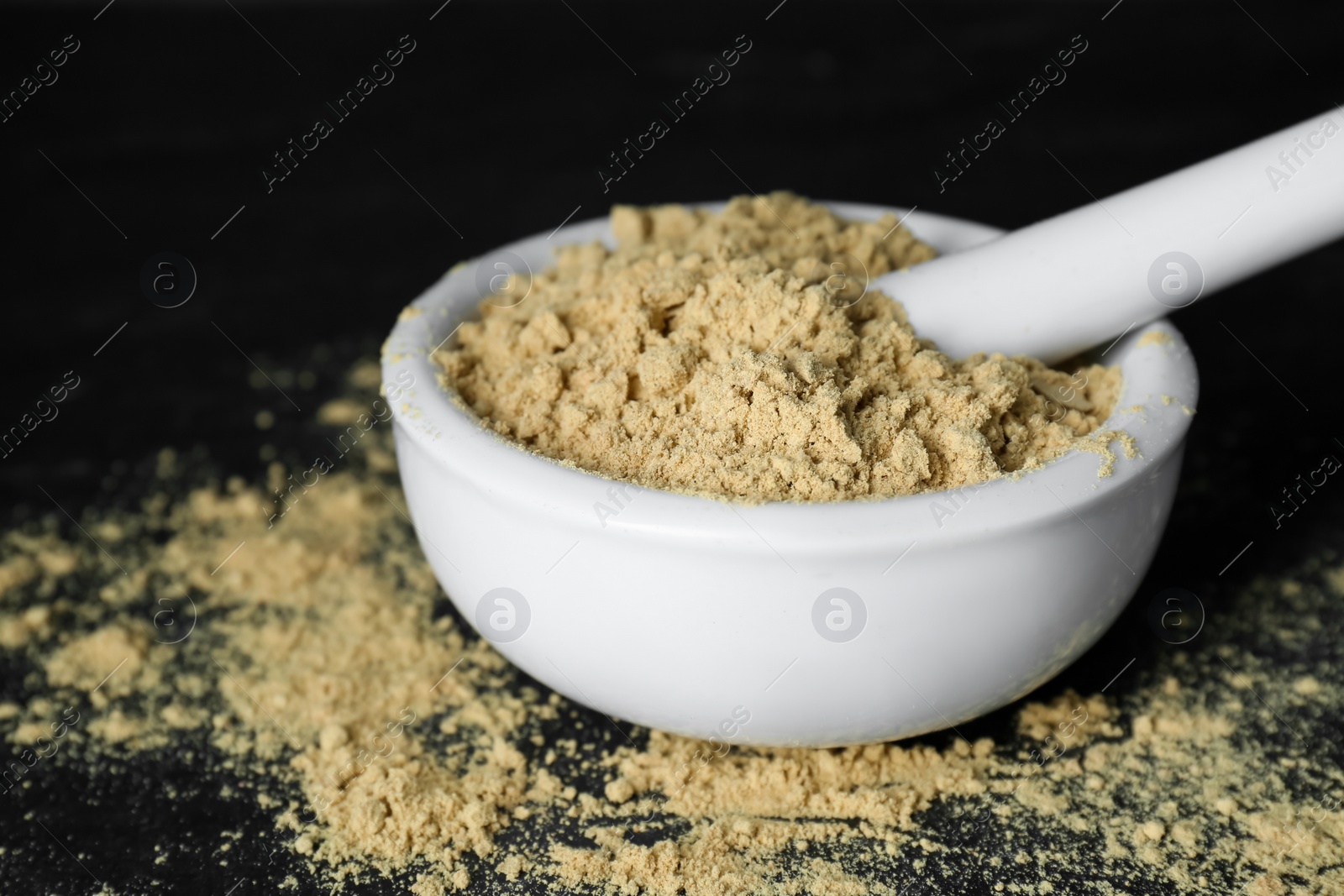 Photo of Mortar with mustard powder on black table, closeup