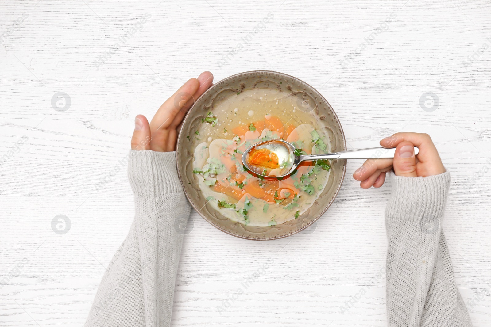 Photo of Man with bowl of soup at white wooden table, top view. Flu treatment