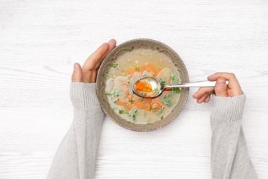 Photo of Man with bowl of soup at white wooden table, top view. Flu treatment