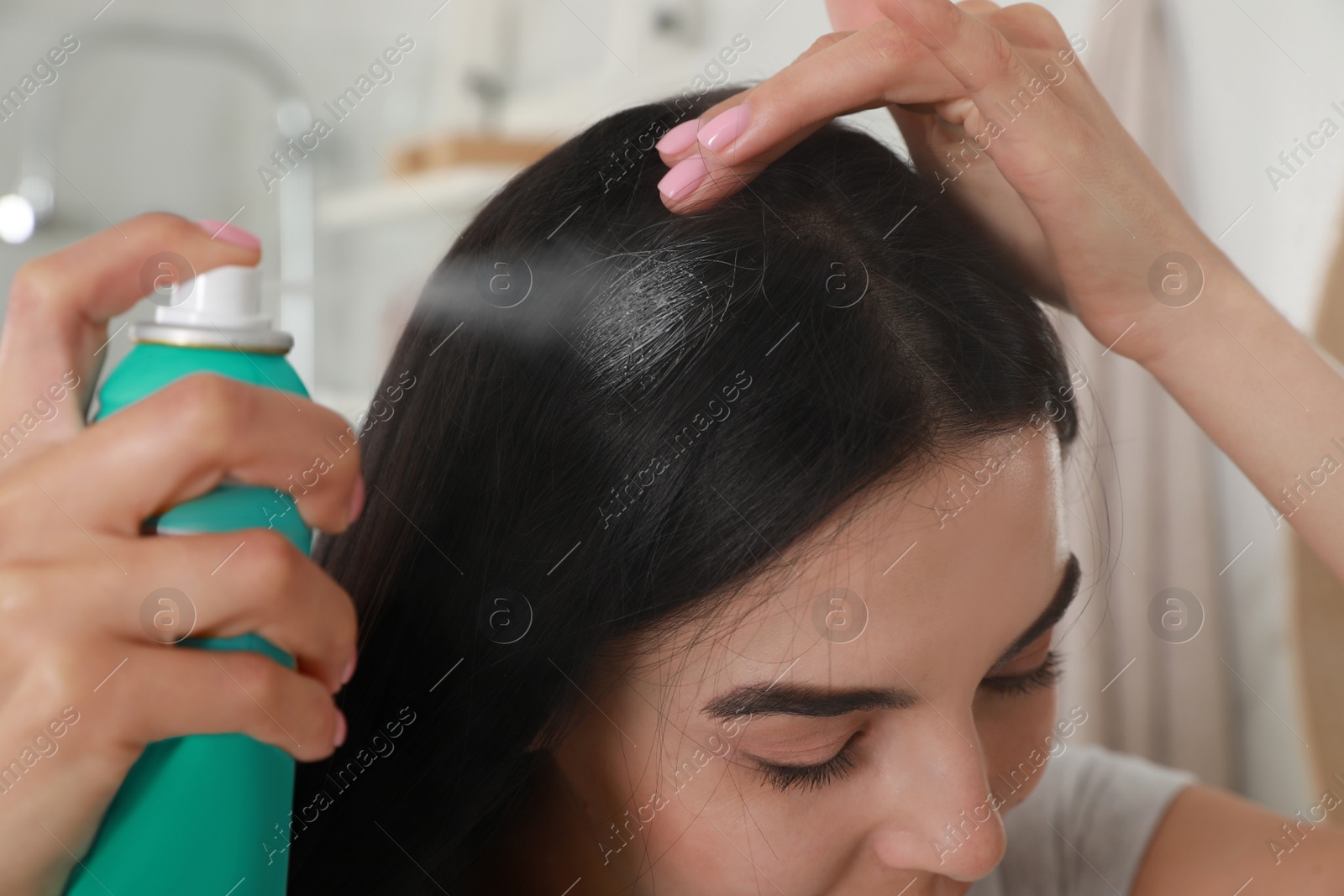 Photo of Woman applying dry shampoo onto her hair indoors, closeup