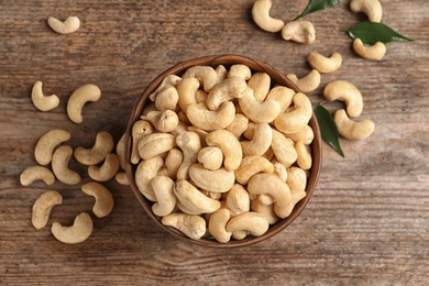 Photo of Tasty cashew nuts in bowl on wooden table, top view