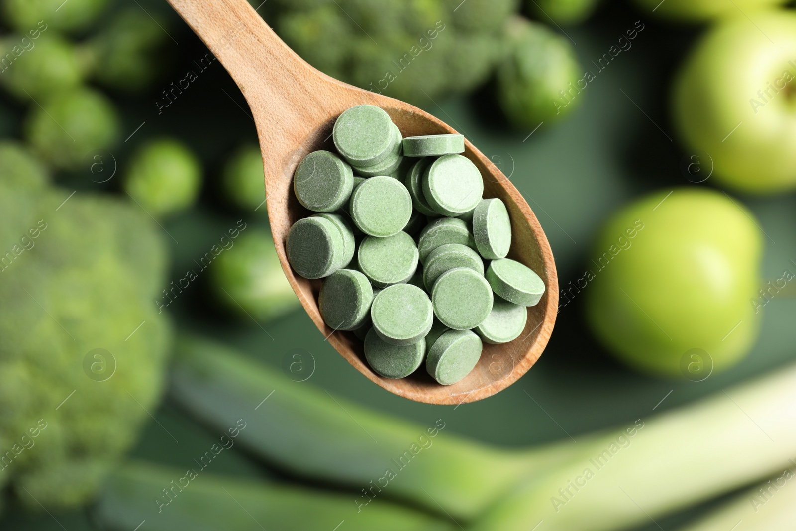 Photo of Wooden spoon with pills on blurred background, closeup. Prebiotic supplements