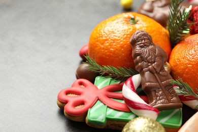 Photo of Chocolate Santa Claus, Christmas sweets and tangerine fruits on grey table, closeup. Space for text