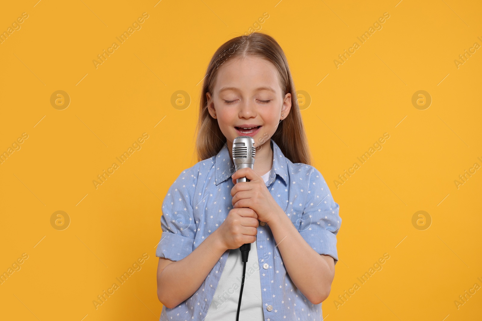 Photo of Cute little girl with microphone singing on yellow background