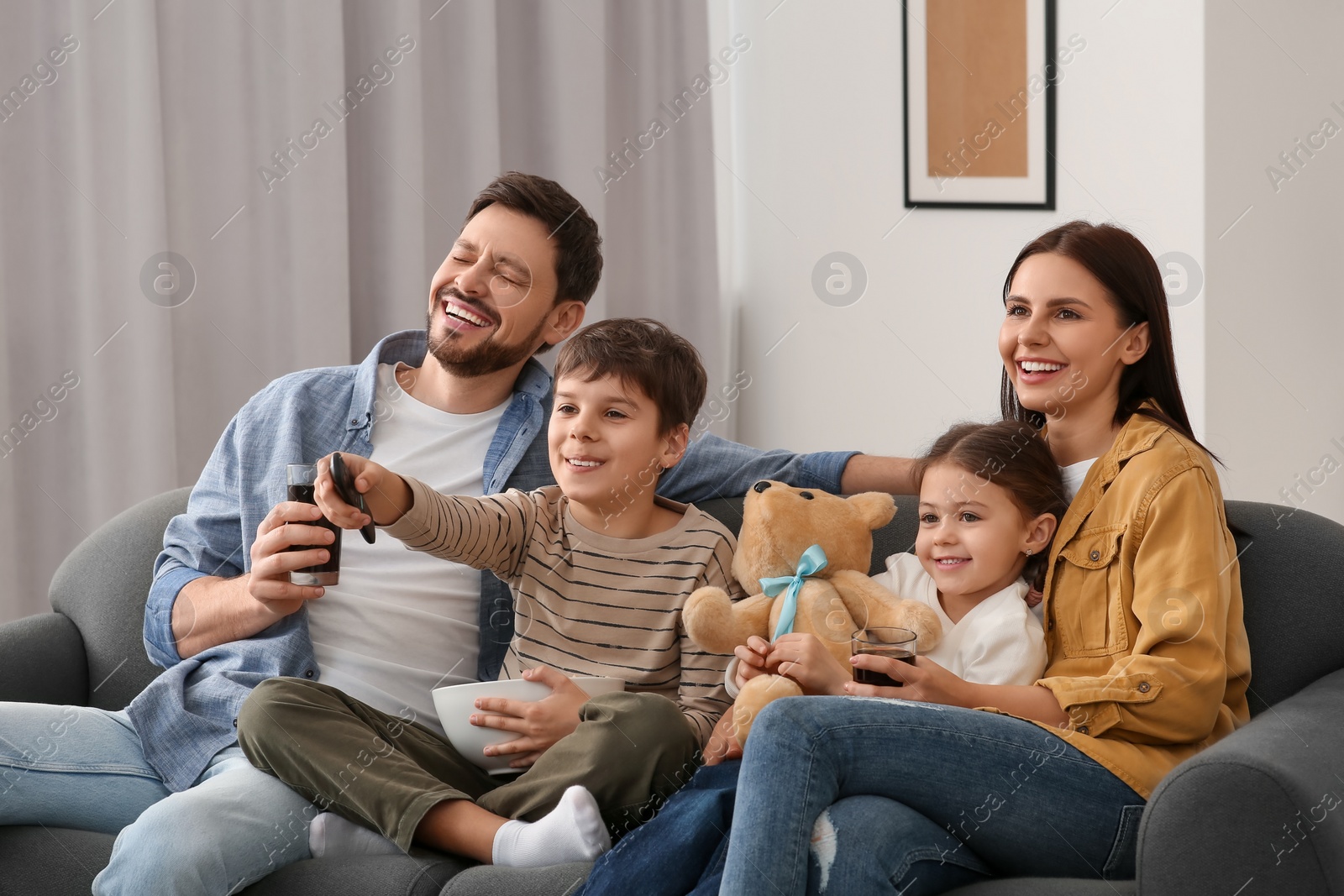 Photo of Happy family watching TV at home. Son changing channels with remote control