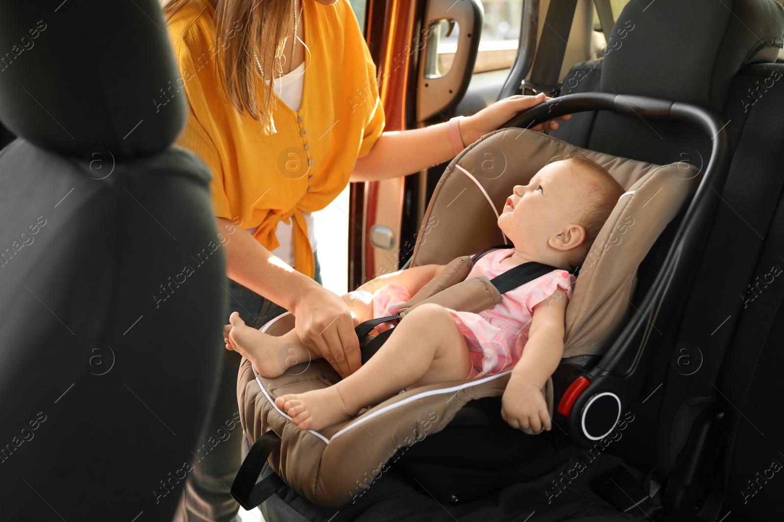 Photo of Mother fastening baby to child safety seat inside of car