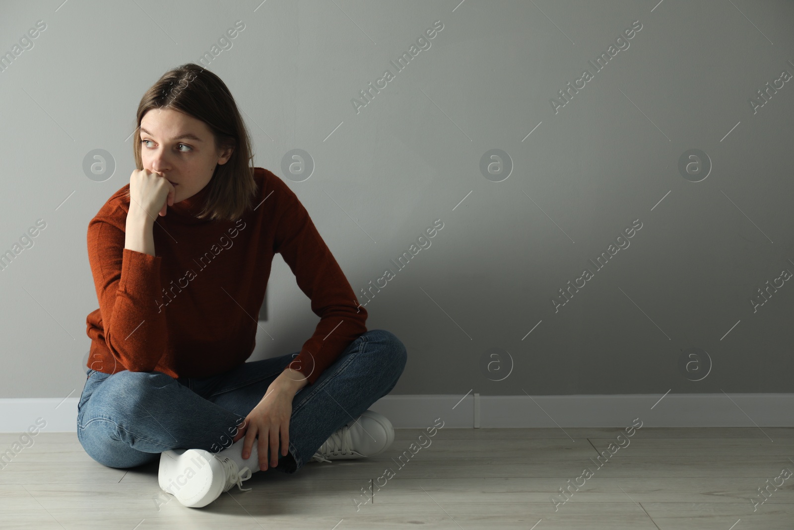 Photo of Sad young woman sitting on floor near grey wall indoors, space for text