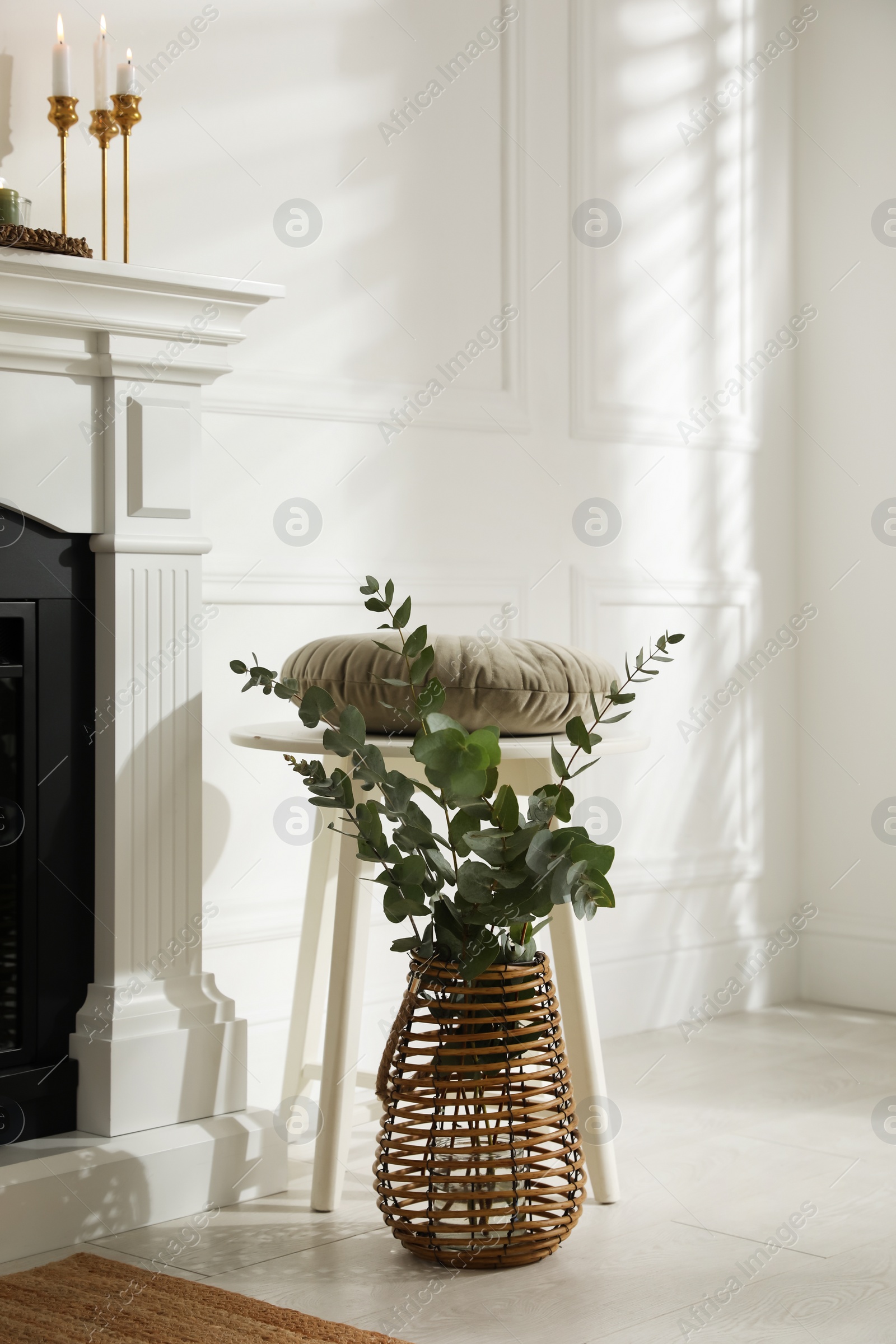 Photo of Beautiful eucalyptus branches in vase and stool near fireplace indoors