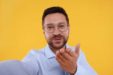 Man taking selfie and blowing kiss on yellow background