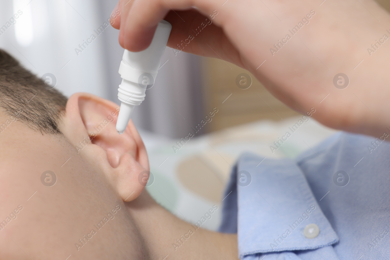 Photo of Man using ear drops indoors, closeup view