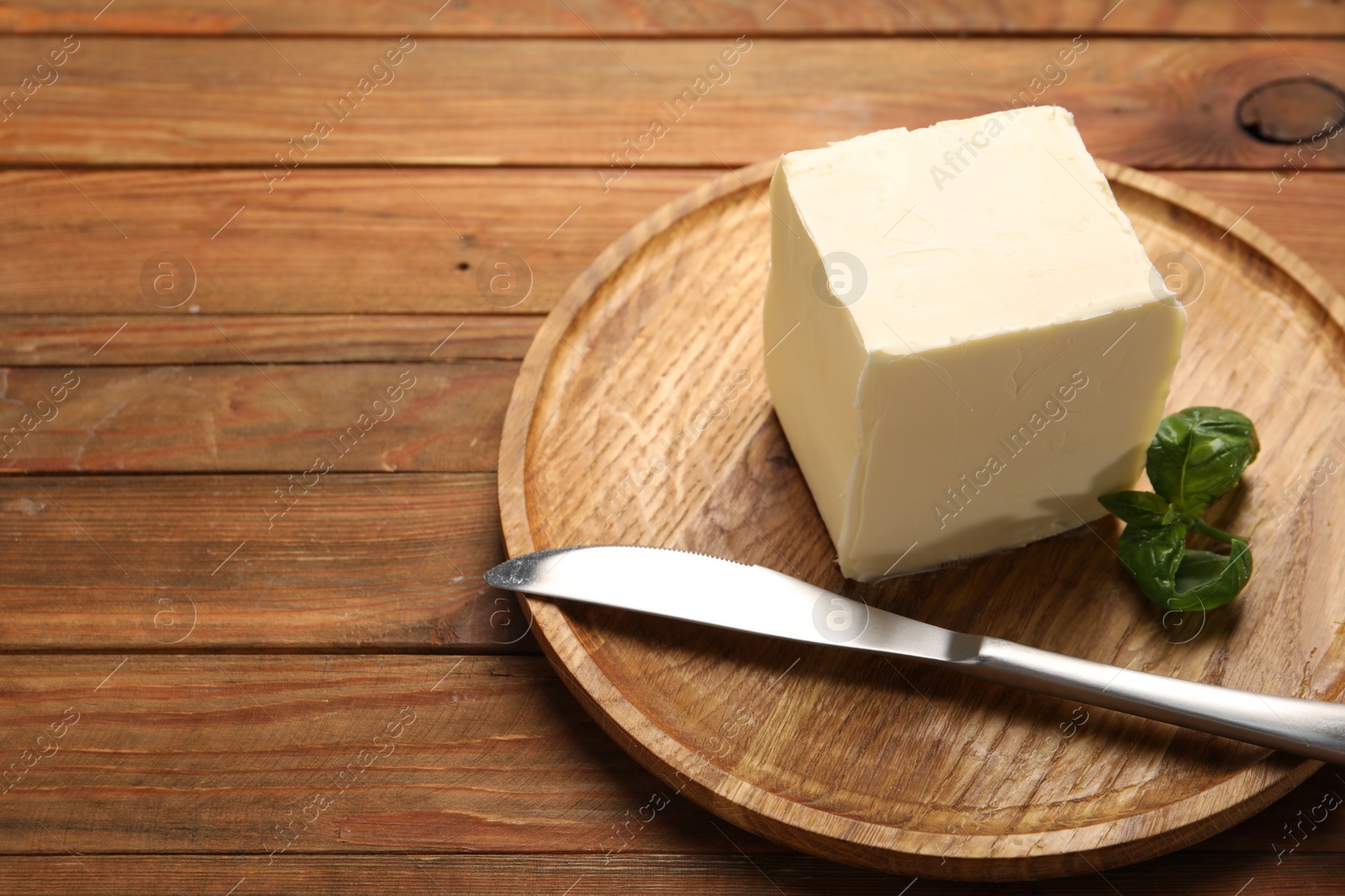 Photo of Block of tasty butter, knife and basil on wooden table. Space for text