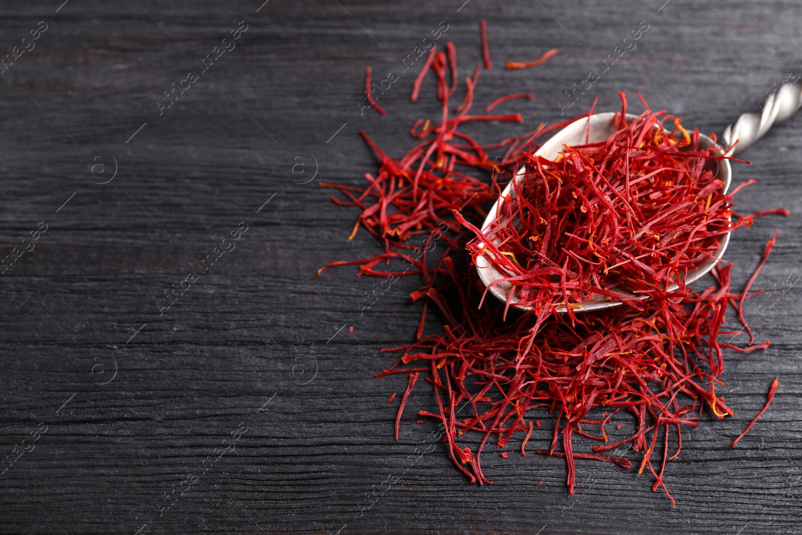 Photo of Dried saffron on black wooden table, closeup. Space for text