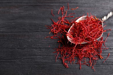 Photo of Dried saffron on black wooden table, closeup. Space for text