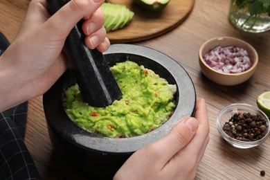 Woman preparing delicious guacamole at wooden table, closeup