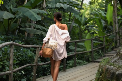 Photo of Young woman walking in green tropical park, back view