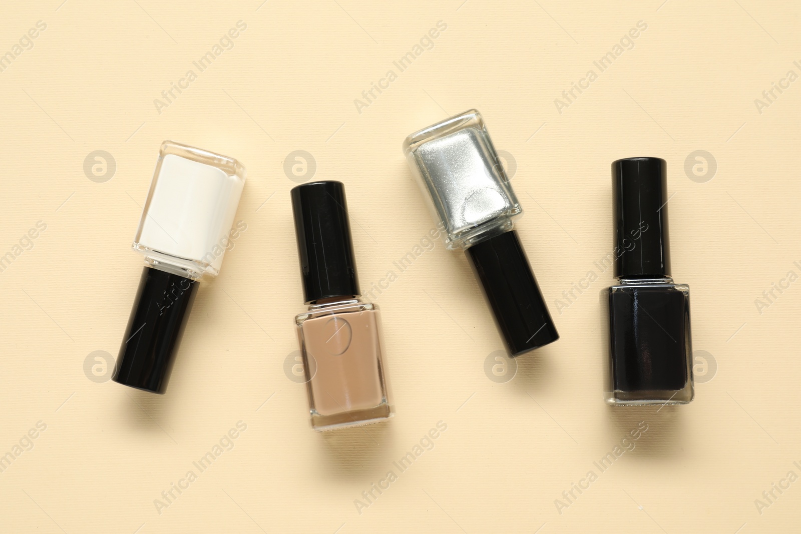 Photo of Bright nail polishes in bottles on beige background, flat lay