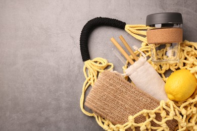 Fishnet bag with different items on grey table, top view and space for text. Conscious consumption