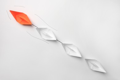 Group of paper boats following orange one on white background, flat lay. Leadership concept