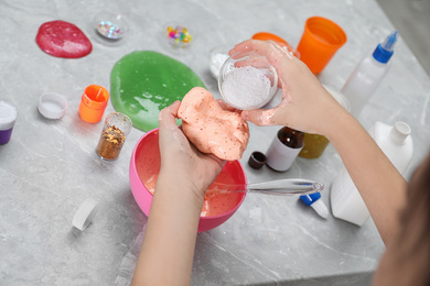 Photo of Little girl adding decorative balls to homemade slime toy at table, closeup