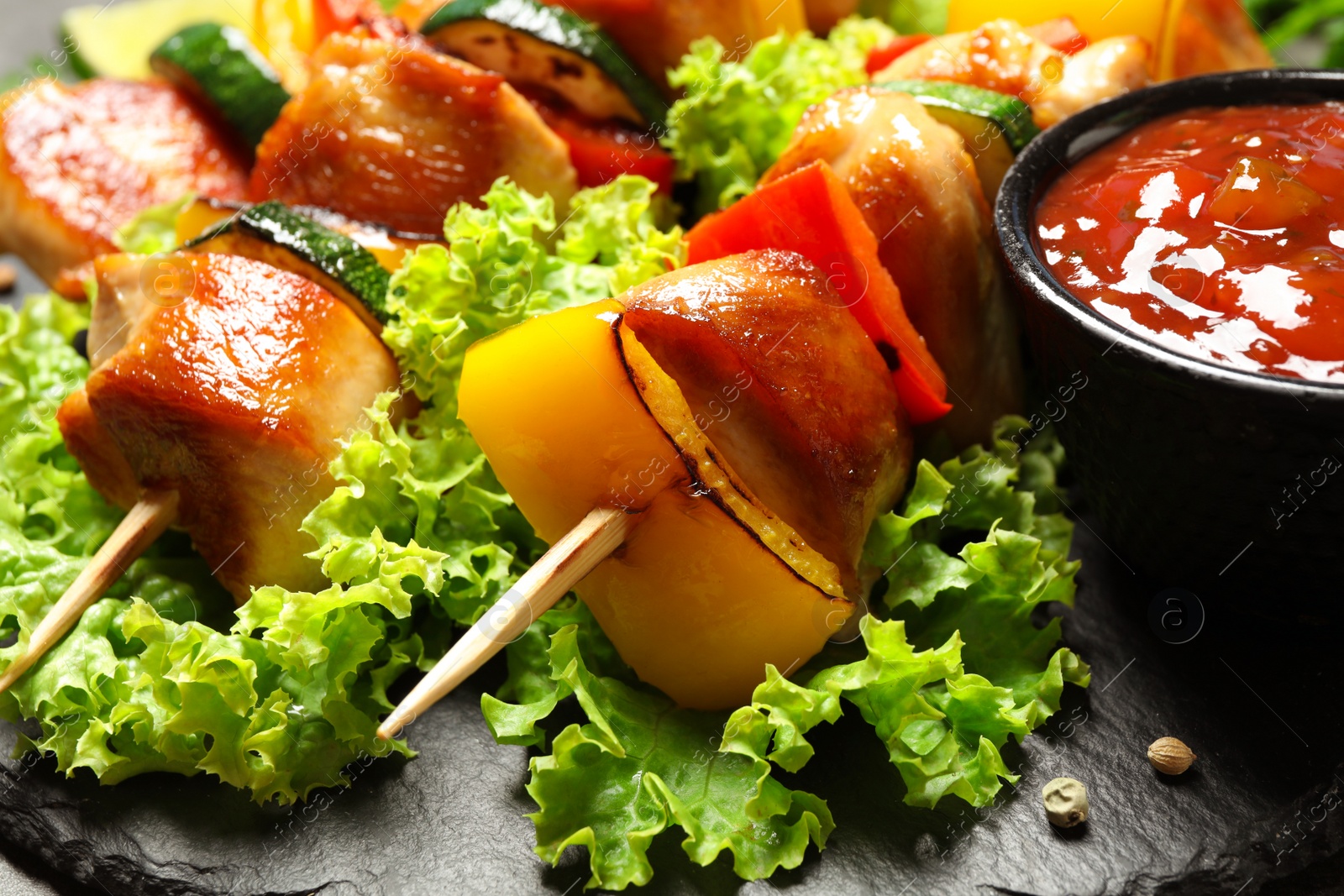 Photo of Delicious chicken shish kebabs with vegetables on slate plate, closeup