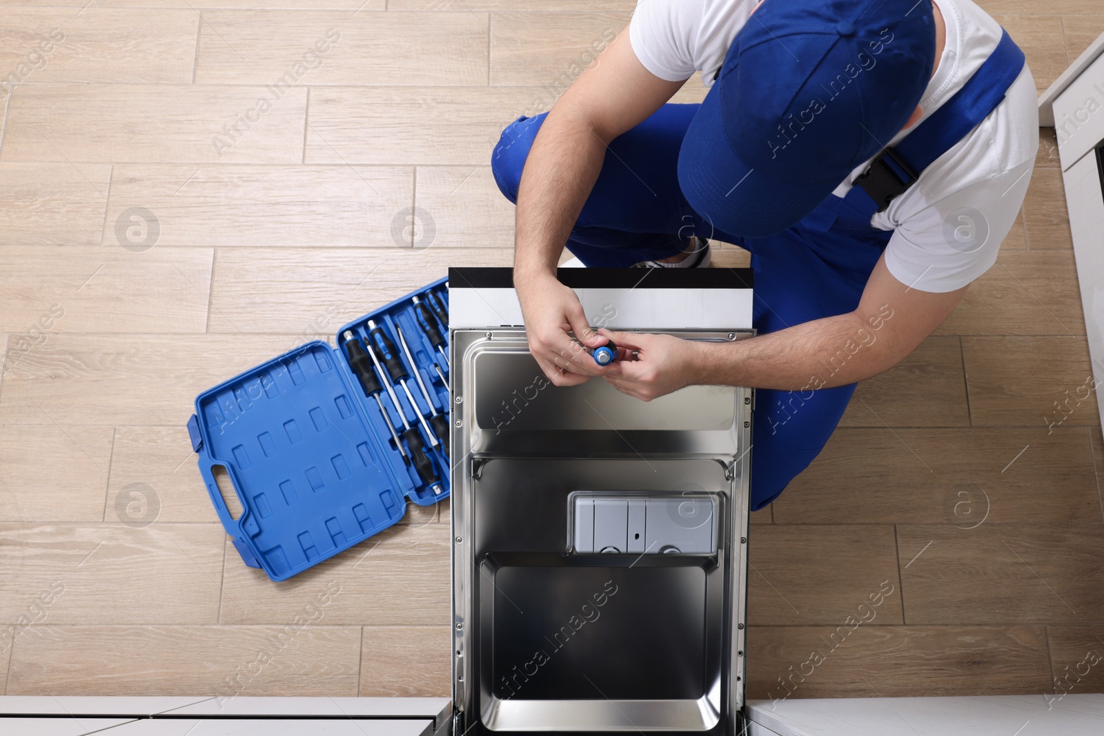 Photo of Serviceman repairing dishwasher's door with screwdriver indoors, above view